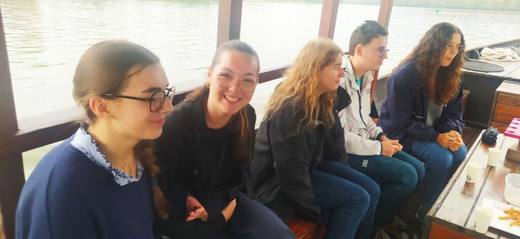 On peut voir 5 participants savourant un apéro posé sur une table basse devant eux. Seule une fille regarde en souriant vers l'objectif. On peut apercevoir de l'eau derrière eux et on devine qu'ils ont sur un bateau