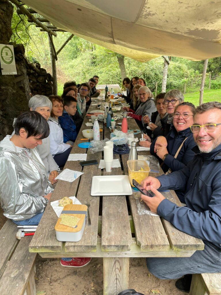 Repas de retrouvaille prise au bout d'un table en bois. Les personnes sont assises des deux côtés de la table sur des bancs en bois